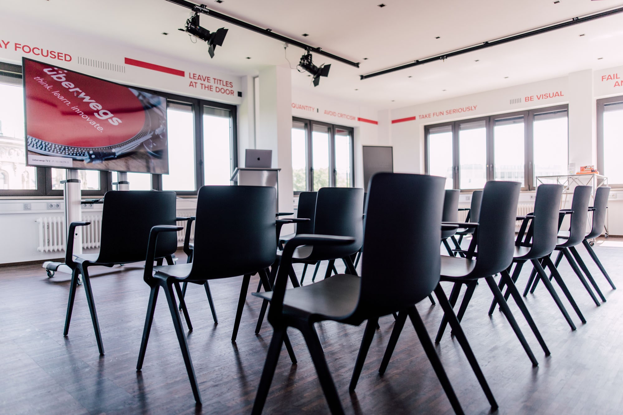 Ein Konferenzraum mit schwarzen Stühlen, einem großen Bildschirm mit der Aufschrift "überwegs" und inspirierenden Sprüchen an den Wänden
