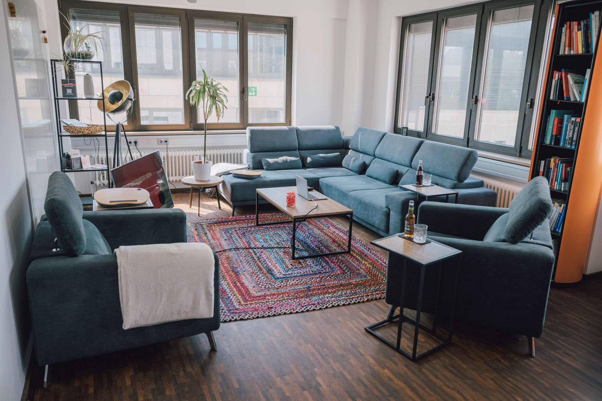 Ein modernes Wohnzimmer mit einer großen Couch, Sessel, einem Couchtisch, Pflanzen und Bücherregalen