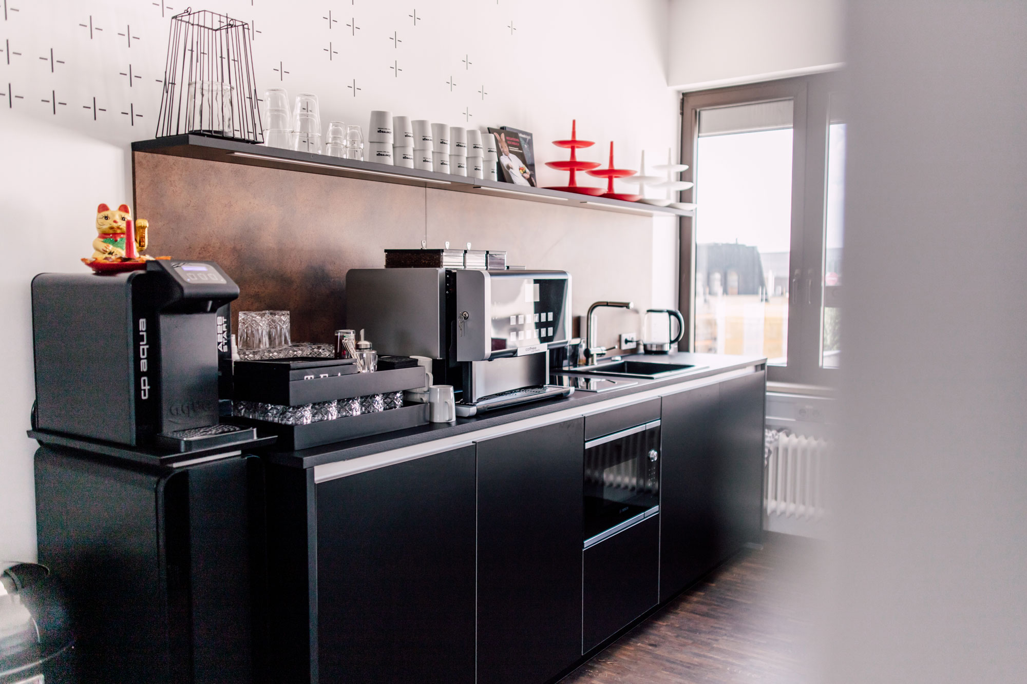 Die moderne Kücheneinrichtung zeigt eine Kaffeemaschine, Gläser und Geschirr auf einem schwarzen Küchenblock